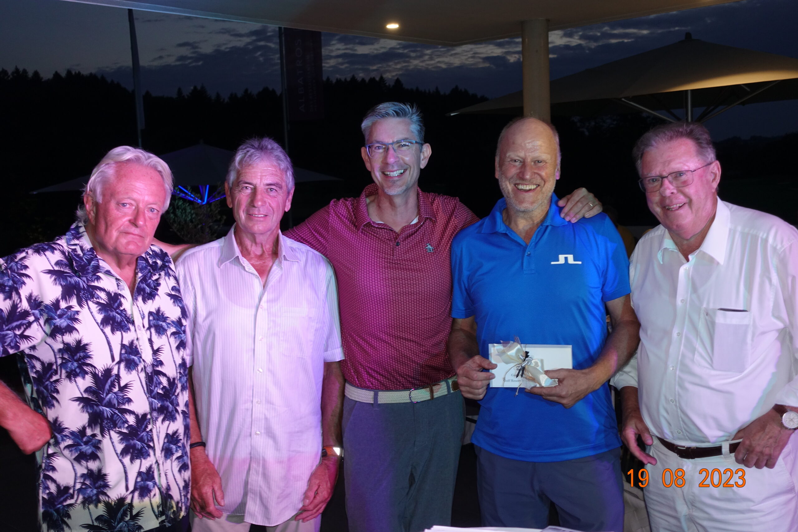 Preisverleihung: Gewinner im blauen Polo mit Kuvert zwischen den Gastgebern