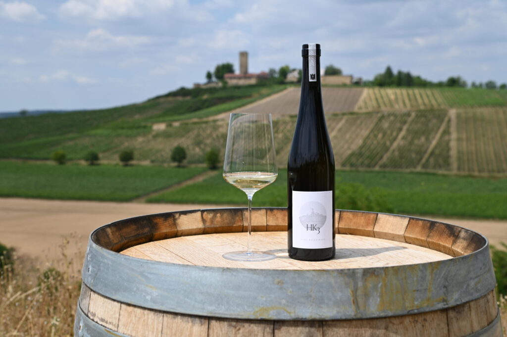 Flasche HK3 und Weinglas auf einem Fass vor Weinbergen und Burg Ravensburg