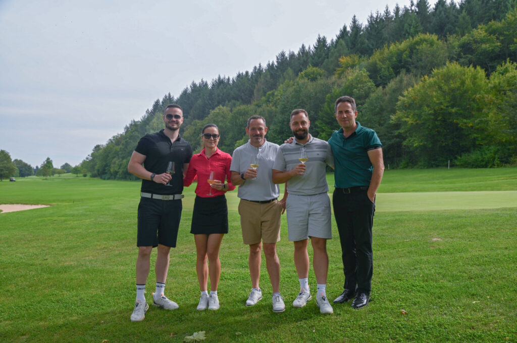 Fünf Golfer mit Weingläsern auf dem Fairway vor Wald