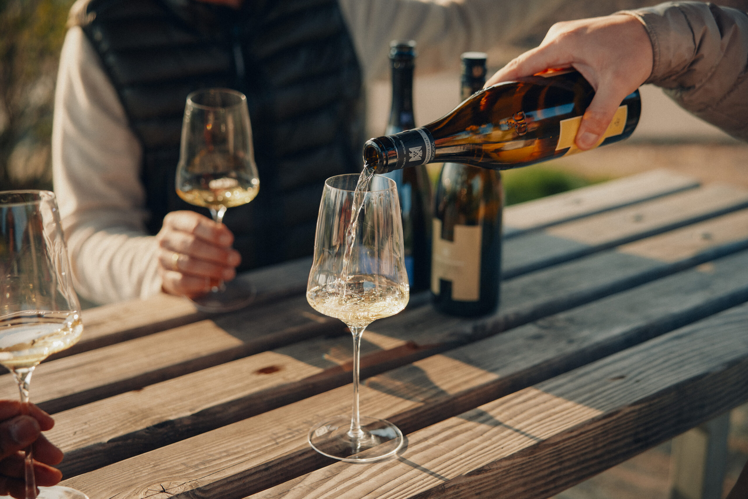 Weißwein wird an einem Holztisch im Freien in Gläser eingeschenkt