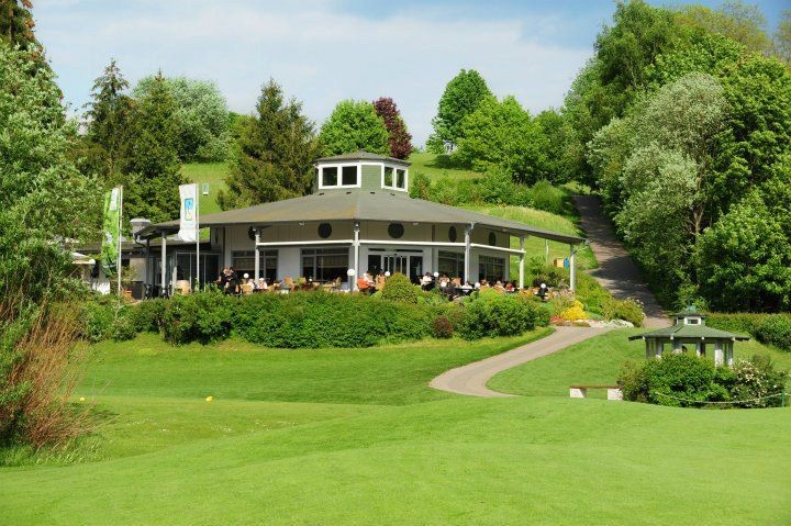 Altes Clubhaus von 1994 mit Terrasse und Gästen am Golfplatz