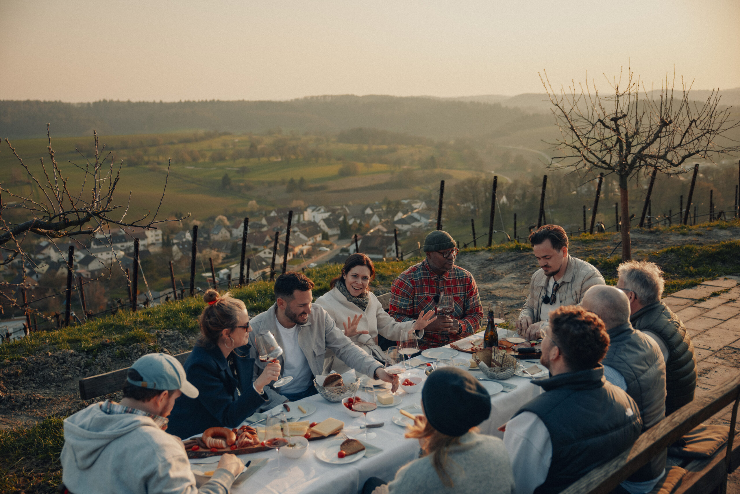 Gruppe an einer langen Tafel im Weinberg mit Blick über das Tal bei Abendlicht