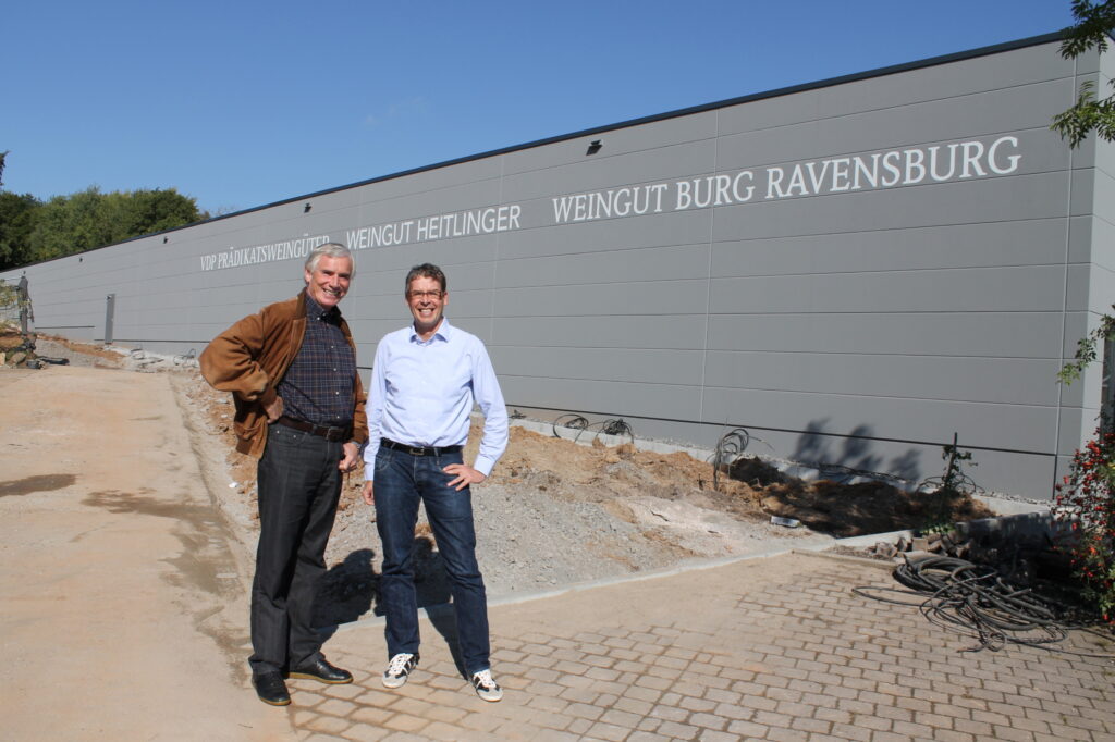 Zwei Männer vor dem neuen Gebäude mit Schriftzug Weingut Heitlinger und Weingut Burg Ravensburg