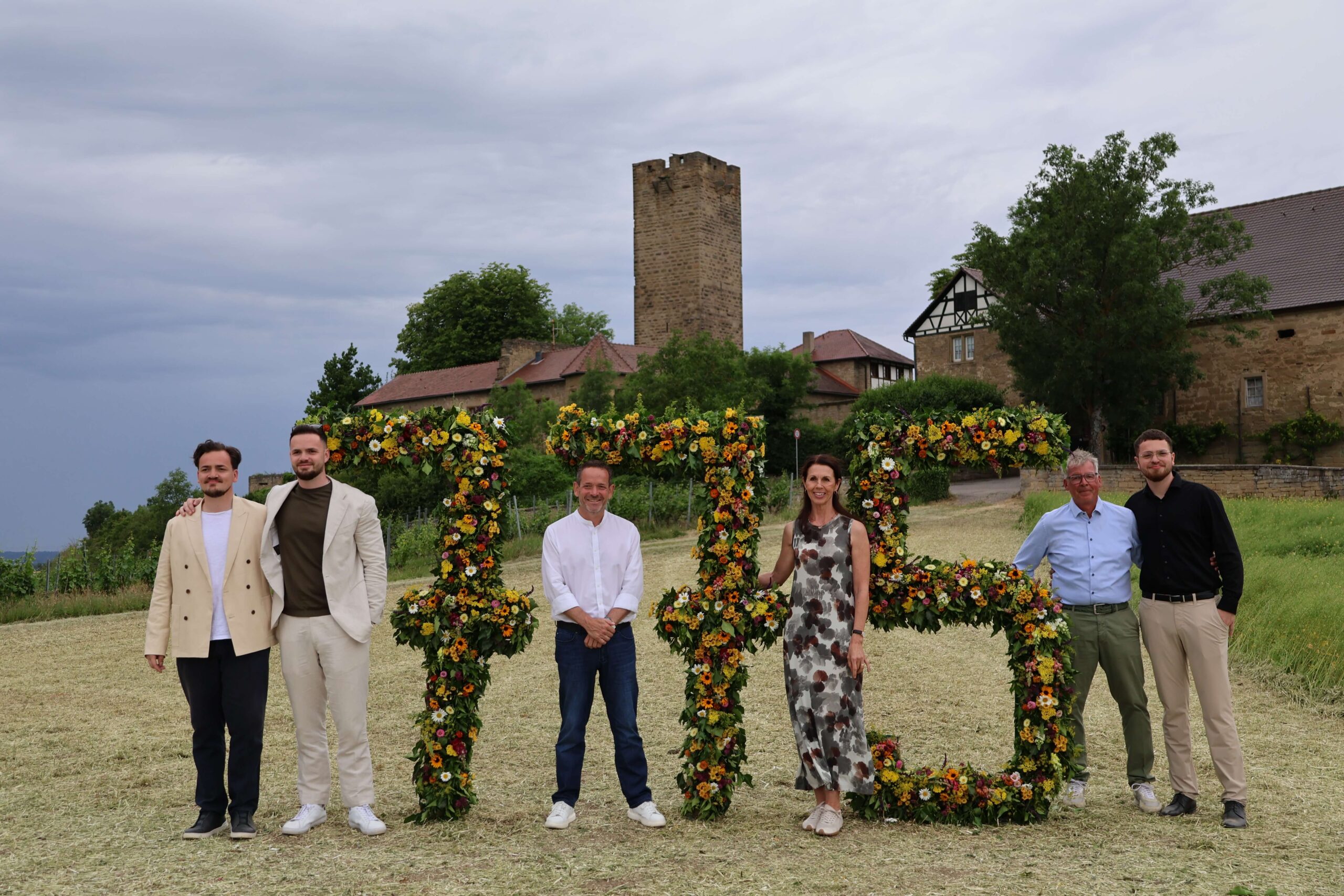 Sieben Personen mit großen Blumenziffern „775“ vor dem Turm der Burg Ravensburg
