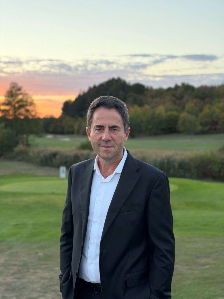 Arif Arifi im dunklen Sakko vor dem Golfplatz bei Abendhimmel