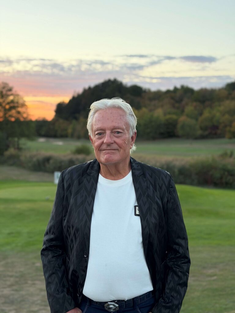 Helmut Dotziger in schwarzer Jacke vor dem Golfplatz bei Sonnenuntergang