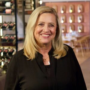 Elvira Fritscher lächelnd in schwarzer Bluse vor Weinregalen im Restaurant