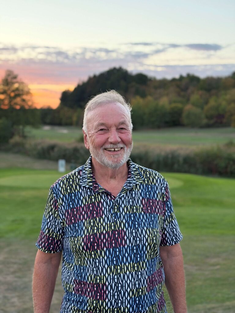 Peter Hans im bunten Poloshirt vor dem Golfplatz bei Abendlicht