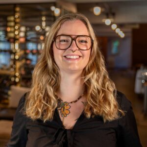 Lächelnde Mitarbeiterin mit Brille und langen blonden Locken im Restaurant
