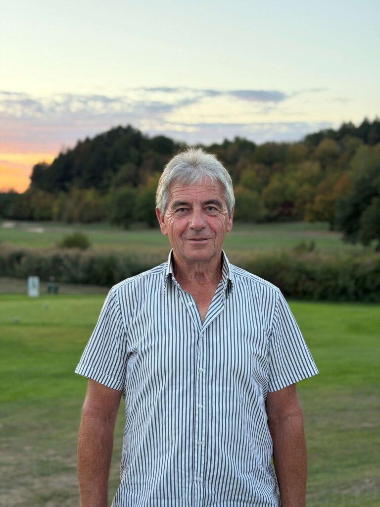 Harald Knaus im gestreiften Hemd vor dem Golfplatz bei Sonnenuntergang