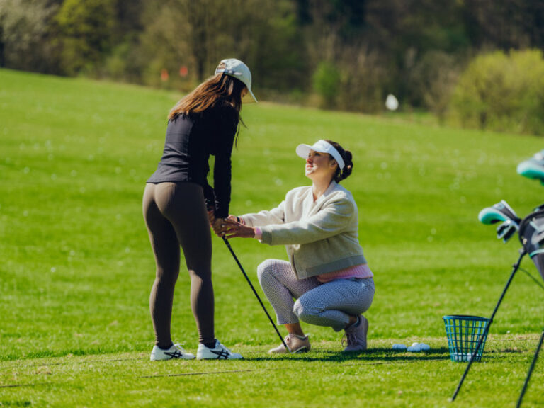 Trainerin korrigiert den Schwung einer Golfspielerin auf der Driving Range